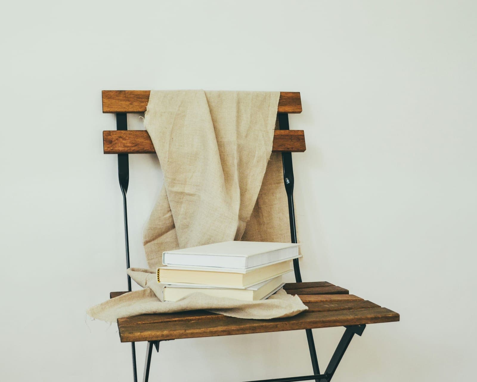 A wooden chair draped with a linen throw, a small stack of plain cream books on its seat.